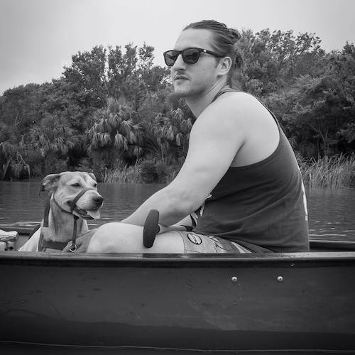 Man wearing sunglasses sitting in a boat with his dog